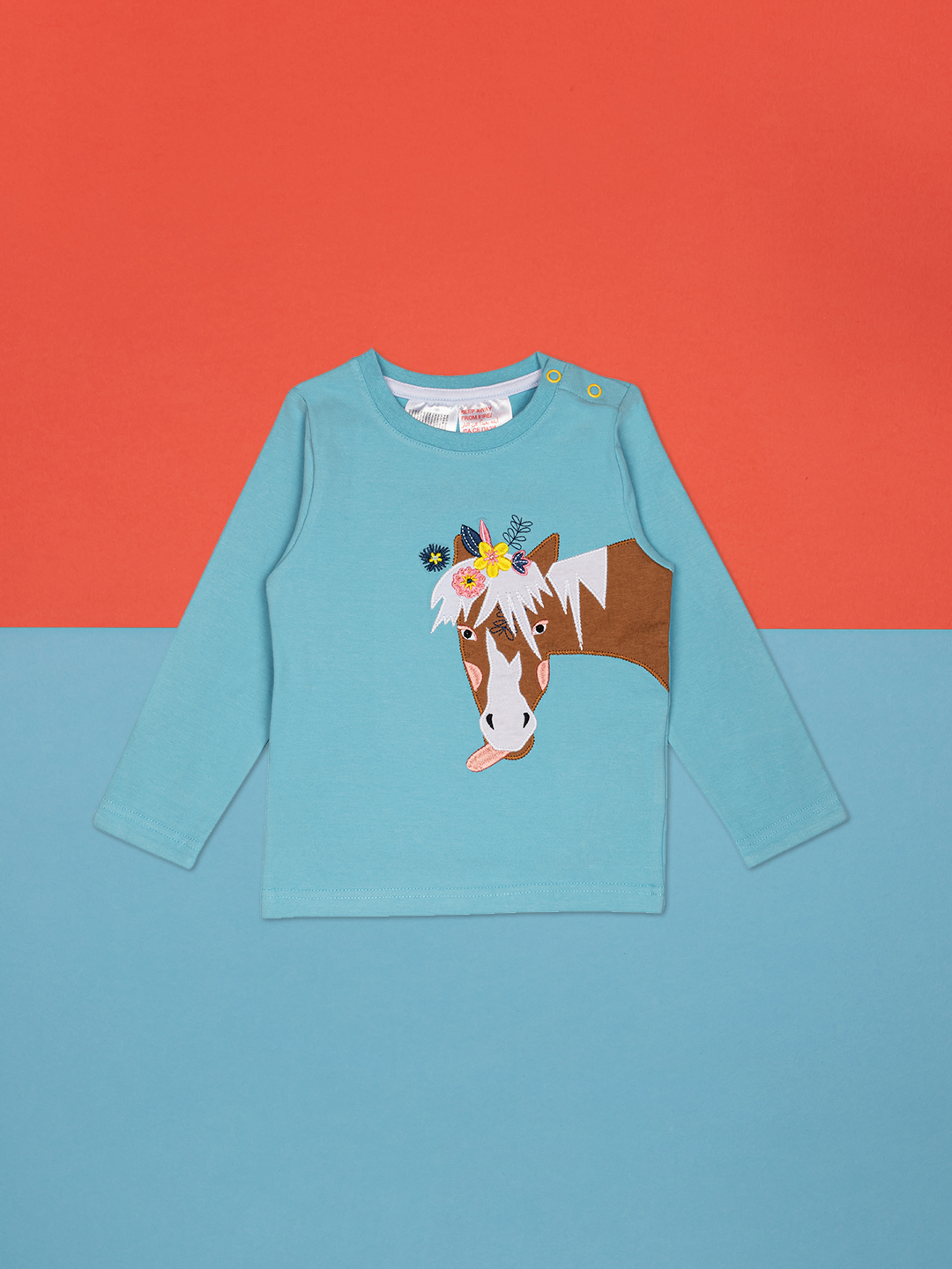 light blue long sleeved top with a brown horse face and neck with a white mane, sticking out a tongue with pretty flowers on the top of her head