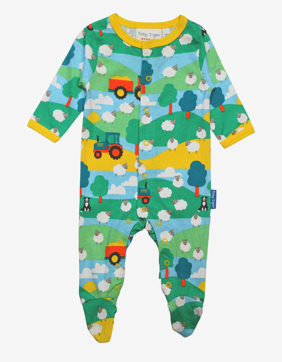 babygrow with farm print featuring tractors and sheep on a green and blue nature background with yellow lining around neckline and sleeves