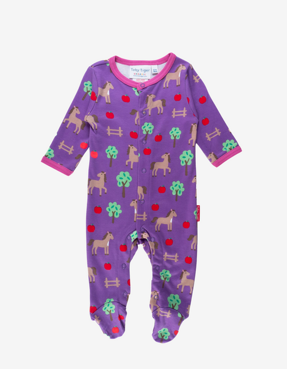 purple babygrow with a horse print featuring fencing, apples and trees and pink lining around the neckline and sleeves